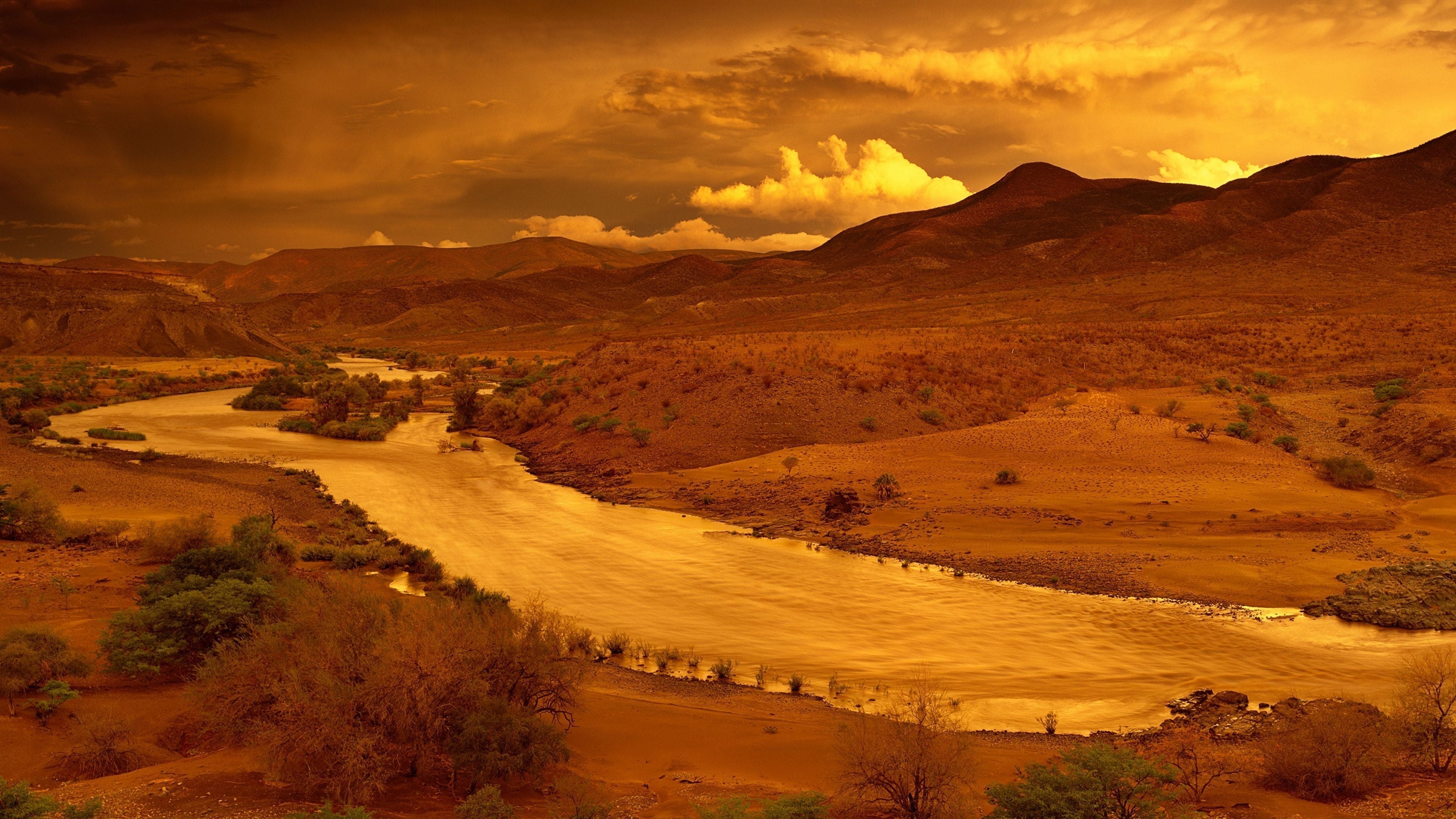 Fine art landscape of a winding river through an arid valley under a dramatic golden sky, capturing the beauty of the African wilderness