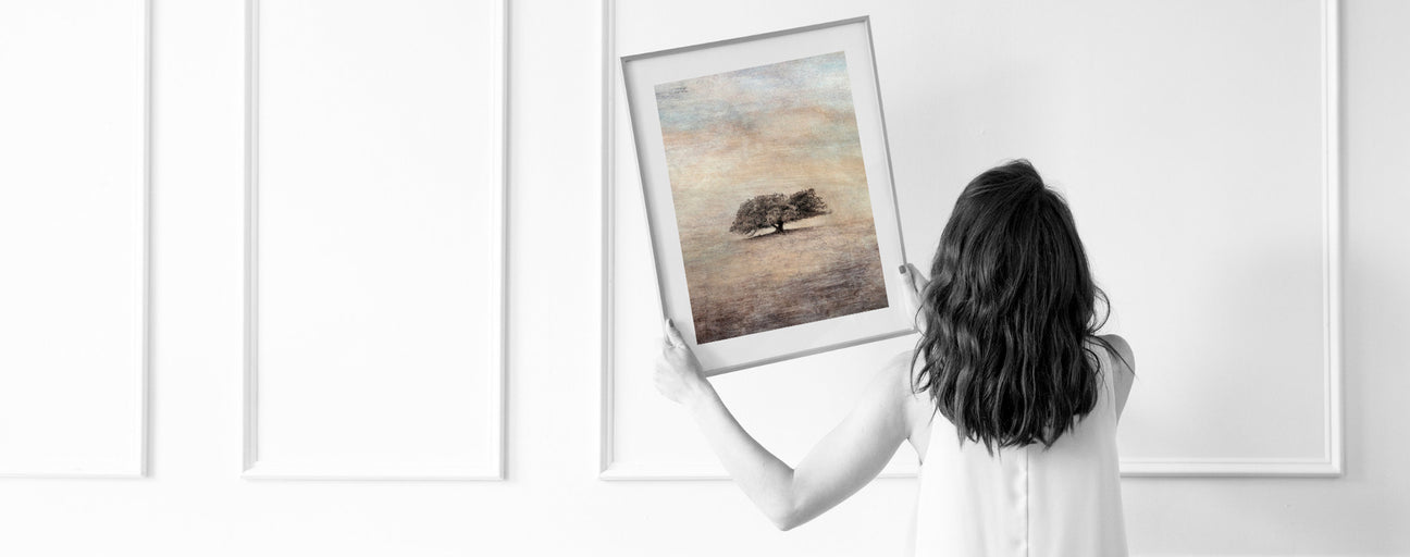 Woman looking at where to hang a framed picture of a tree on a white wall