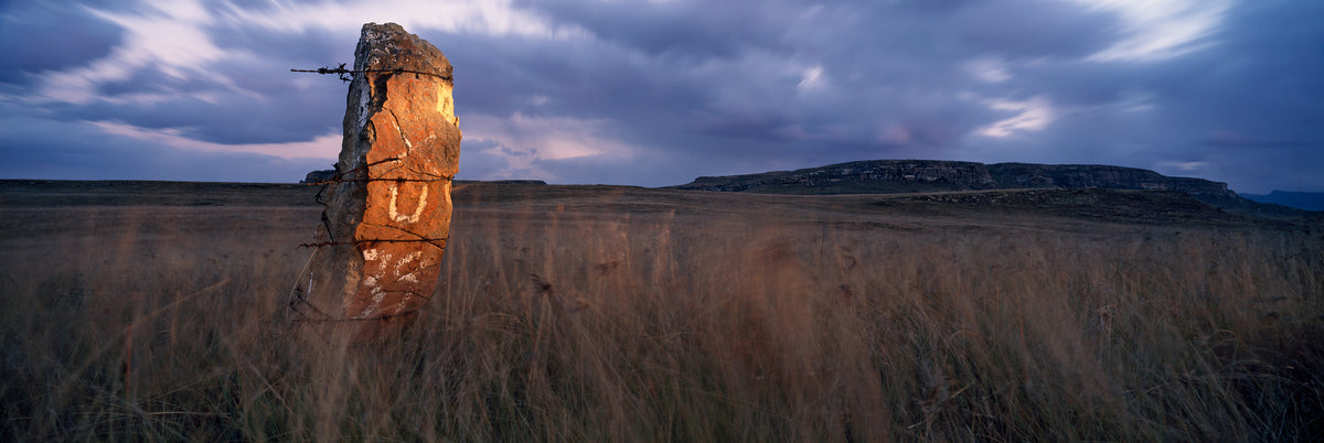 Sandstone Pillar, Free State by Koos van der Lende, a lone sandstone fence post in tall grass under a stormy sky