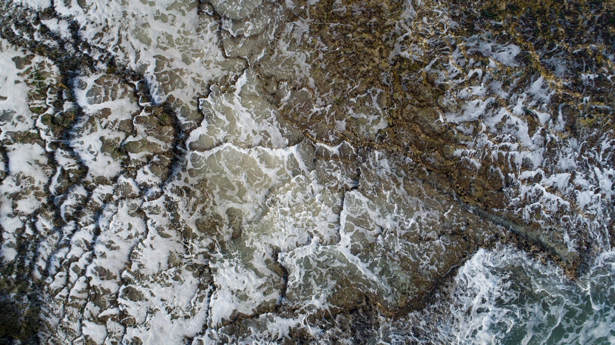From Above | Salt & Pattern by Martin Osner, waves breaking over a rock island, seen from above